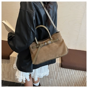 Detail of suede baguette bag with buckle strap and dual handles in autumn brown tones