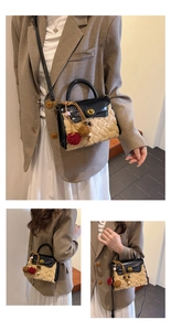 Detail of plush heart-embossed bag with gold rotary lock and colorful pompom charm