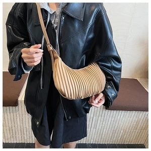 Close-up of pleated beige croissant bag with adjustable shoulder strap on model
