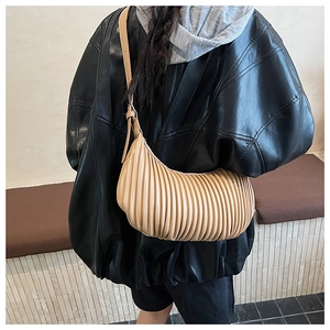 Detail view of beige pleated crescent hobo bag worn over a black leather jacket
