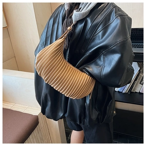 Detail of a beige pleated crescent shoulder bag paired with a black leather jacket