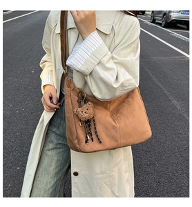 Detail of a brown suede hobo bag with adjustable strap and cute plush bear charm