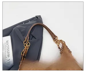 Detail of woven leather edges and golden metal rings on a brown suede shoulder bag