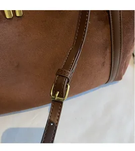 Detail of adjustable strap with gold buckle on brown matte suede crossbody bag