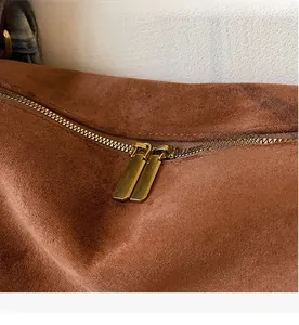 Detail showing smooth double metal zippers on dark brown suede crossbody pillow bag