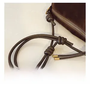 Detail of dark coffee suede shoulder bag showing knotted strap and gold metal zipper hardware