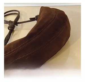 Detail of brown suede handbag featuring triple parallel stitching and knotted strap detail