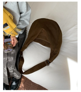 Detail of a dark brown crescent bag on white bedding with a fabric adjustable strap