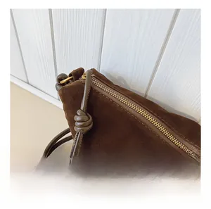 Close-up of smooth metal zipper and knotted strap on dark brown suede crossbody bag