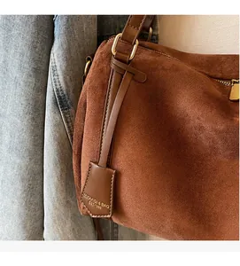 Close-up of brown suede shoulder bag featuring leather strap and branded hangtag