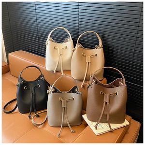 Five assorted bucket bags in lychee leather displayed on a brown sofa with gold hardware
