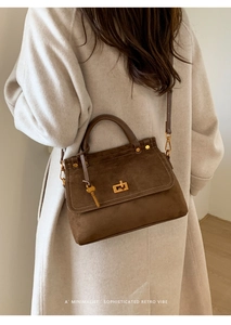 Detail view of retro brown suede handbag with gold lock and adjustable shoulder strap
