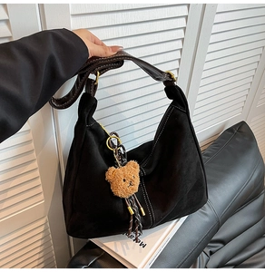Detail of black suede hobo bag with white stitching and cute brown bear pendant
