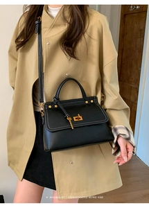 Detail of black leather handbag with white contrast stitching and gold hardware on a model
