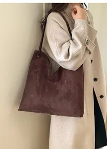 Braune Wildleder-Hobo-Tasche am Model mit beigem Kaschmirmantel in minimalistischem Interieur