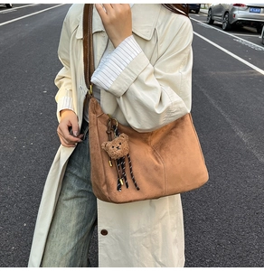 Dettaglio di una borsa hobo in pelle scamosciata marrone con ciondolo a forma di orso