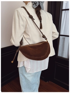 Detail of dark brown suede half-moon crossbody bag with decorative knotted shoulder strap
