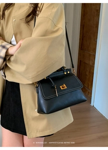 Detail of black trapezoid suede bag with gold clasp and white contrast stitching