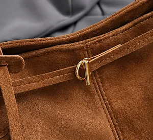 Detailopname van de gouden T-gesp op de bruine suède tas met luxe metalen accent