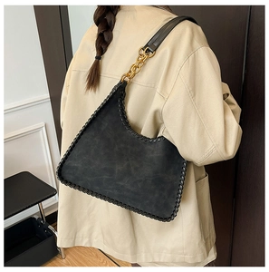 Detail of black tote bag featuring whipstitch edges and gold chain shoulder strap