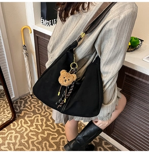 Detail of black canvas crossbody bag with brown strap and plush bear charm on model