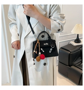 Detail of black leather Kelly-style handbag featuring a metal turn-lock and colorful charms