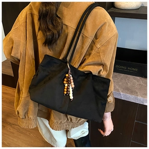 Détail d'un grand sac cabas en nylon noir avec breloque en bois porté à l'épaule