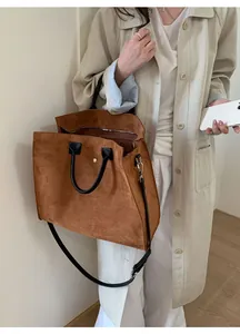 Borsa tote marrone in pelle scamosciata con manici neri portata a tracolla da una modella