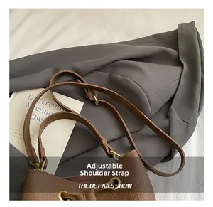 Detail of adjustable strap with gold buckles on brown lychee grain bucket bag
