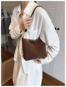 Detail of a brown suede bucket bag featuring golden zippers on a stylish model