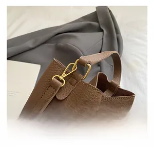 Detail of gold metal hooks and pebble leather texture on a brown bucket bag
