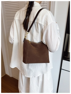 Detail view of brown suede shoulder bag with gold hardware on a model in white outfit
