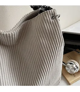 Detail of grey corduroy tote bag featuring silver eyelets and checkered woven strap