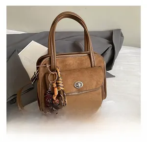 Detail of a brown vintage briefcase with suede textures, metal turn-lock, and woven charm