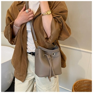 Close-up of taupe bucket bag with drawstring closure and litchi texture on a model