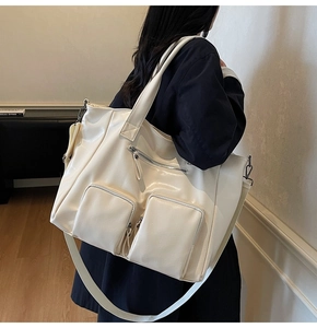Detail of cream white tote bag featuring front utility pockets and detachable wide strap