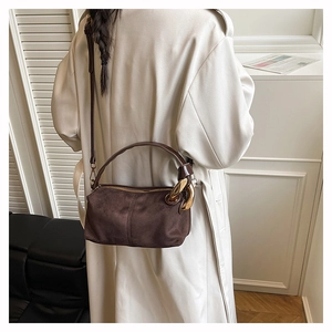 Detail of a brown suede cylinder shoulder bag with a bold gold chain on a model