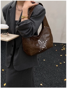 Detail of dark brown faux leather hobo bag with silver star rivets on grey suit