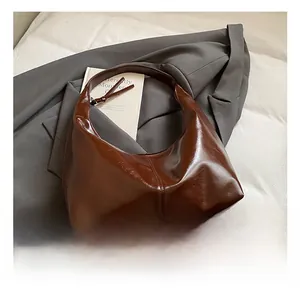 Detail of a dark brown oil-wax leather hobo bag with glossy texture and zipper close