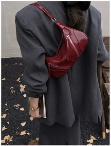 Street style view of a dark red patent leather crescent crossbody bag with zippers