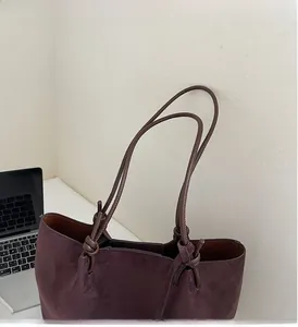 Detail of burgundy suede tote bag with durable dark brown leather handles and knot design