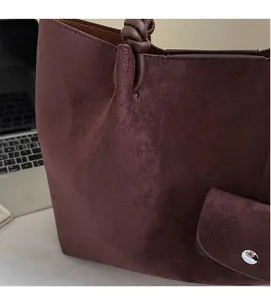Detail of burgundy suede tote bag featuring knot handle design and magnetic snap pocket