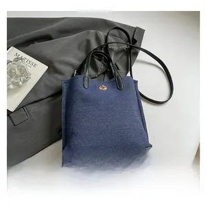 Detailed shot of dark blue denim tote bag with black leather handle and gold twist lock