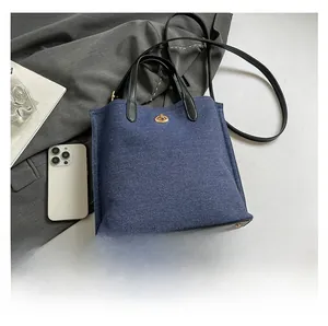 Detailed macro view of denim tote bag showing metal twist lock and black leather trim