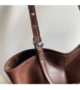 Detail of adjustable leather strap with silver buckle on dark brown tote bag