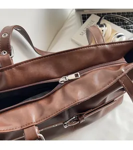 Detail of silver zipper closure and adjustable strap on a brown faux leather tote bag