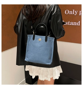 Detailed shot of a blue denim tote bag with leather handles and gold twist-lock buckle