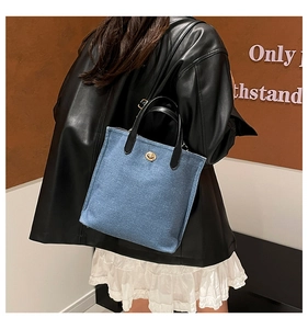 Détail d'un sac cabas en denim avec anses en cuir noir et fermoir rotatif doré