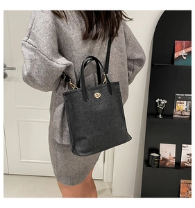 Detail of black textured tote bag featuring gold twist-lock and adjustable leather strap