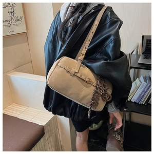 Detail of beige rectangular shoulder bag with woven pendant and adjustable strap
